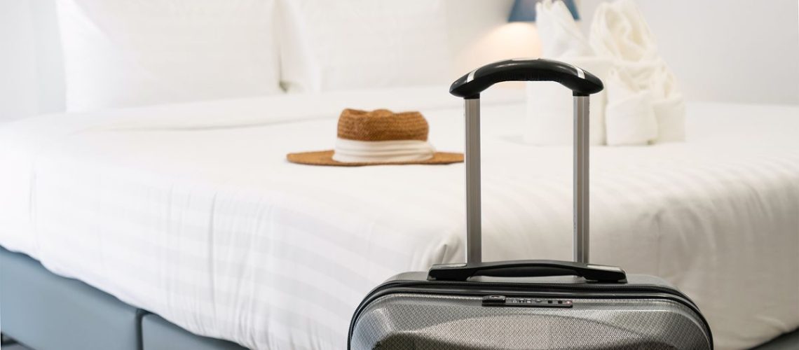A suitcase in front of a mattress in a hotel room