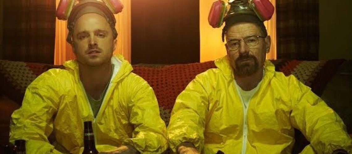 Actors Bryan Cranston and Aaron Paul, wearing yellow hazmat suits, sipping beer on sofa in a scene from Breaking Bad, the hit AMC crime series – here's where to watch and stream seasons 1-5