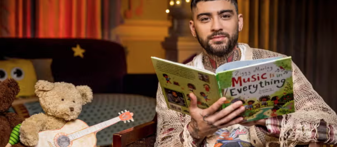 Former One Direction star Zayn Malik sits next to a teddy bear holding a toy guitar to read a