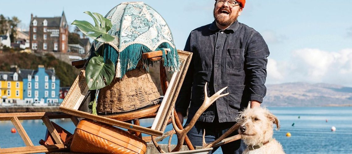 Banjo Beale, wearing red woolly hat and workmanlike denim jacket, carries a wheelbarrow filled with bric-a-brac alongside his faithful dog in BBC's Designing the Hebrides season 2