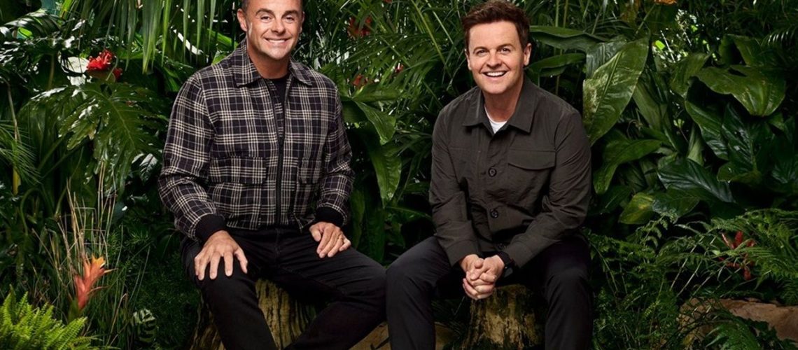 Against lush green foliage, hosts Ant McPartlin and Declan Donnelly sit on tree stumps sporting Cheshire cat grins, anticipating the arrival of the latest celebrity campmates for "I'm a Celeb" 2025.