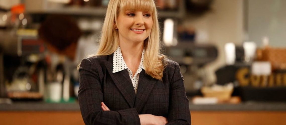 Judge Abby Stone (Melissa Rauch), the lead character in NBC sitcom Night Court season 2, poses with her arms crossed, wearing a dark grey suit and white polka dot shirt.