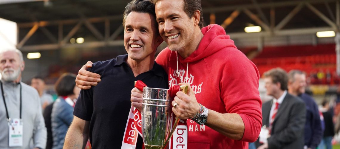 Rob McElhenney and Ryan Reynolds, co-owners of Wrexham AFC, pose for a photo with the trophy following the club's promotion to the Sky Bet Championship during the Sky Bet League One match between Wrexham AFC and Charlton Athletic FC at Racecourse Ground on April 26, 2025 in Wrexham, Wales.