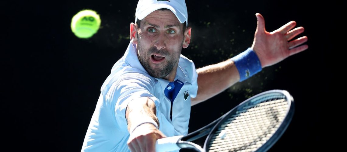 Novak Djokovic of Serbia, wearing white baseball cap and shirt, plays a backhand at the Australian Open 2024 Grand Slam tennis tournament.