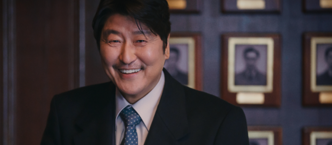 Veteran Korean actor Song Kung-ho plays Park Doo-chill (aka Uncle Samsik) in a dark business suit, smiling in a wood-lined office