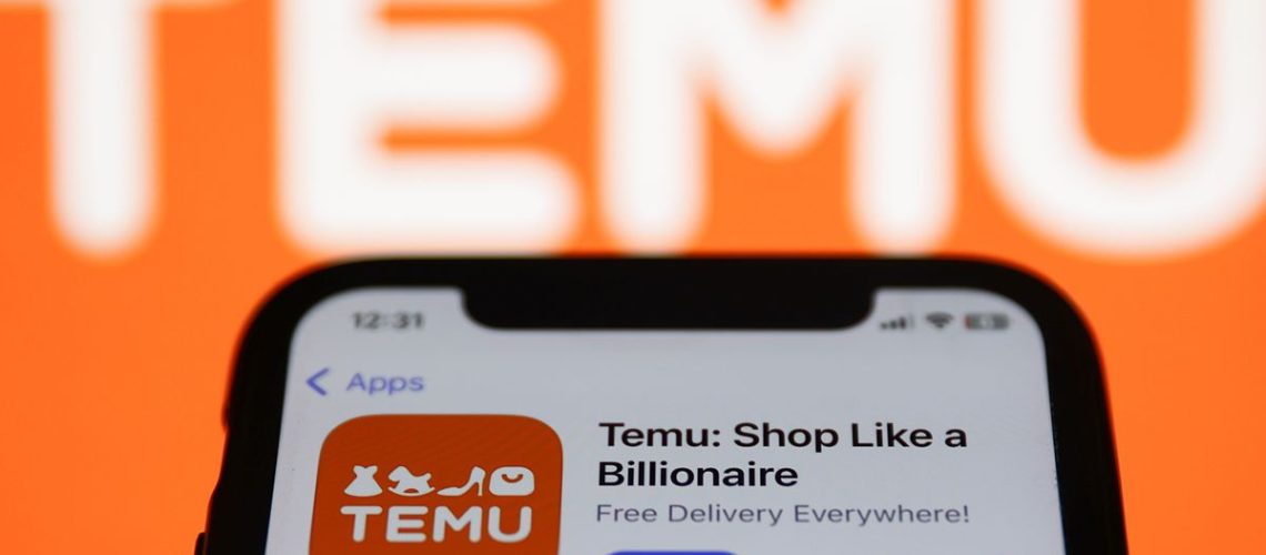 Temu on App Store displayed on a phone screen and Temu logo displayed on a screen in the background ahead of airing of