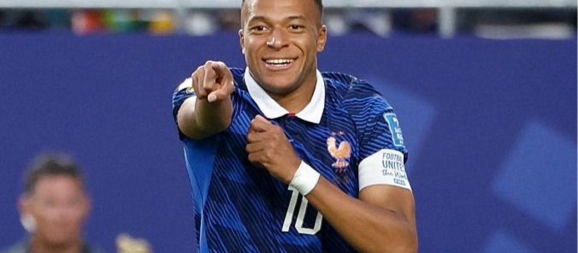 A smiling Kylian Mbappe, wearing blue, points to a team-mate during France's World Cup 2026 campaign.