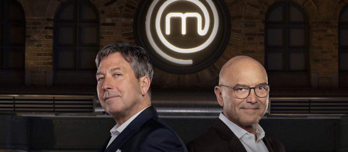 Presenters John Torode and Gregg Wallace standing beneath the MasterChef UK crest