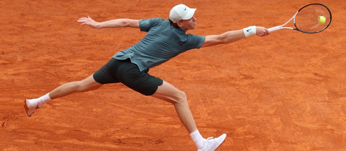 Jannik Sinner wearing white cap and green top stretches for the ball ahead of the 2026 French Open Roland Garros tennis