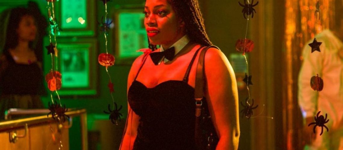 Queenie Jenkins (Dionne Brown) wearing a white collar, bow-tie and black dress at a Halloween party