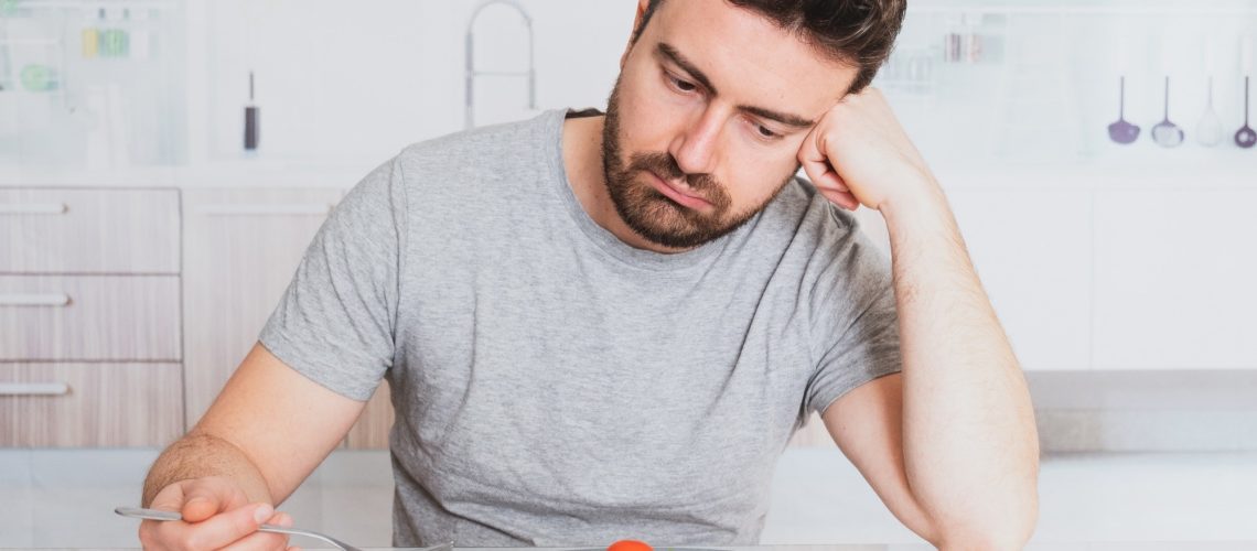 Man looking depressed and stressed with a plate of vegetable and a fork in his hands