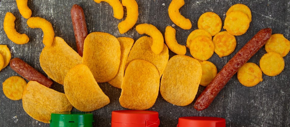 Fast food, unhealthy snacks, chips, sausages, and harmful sauces on a black background.