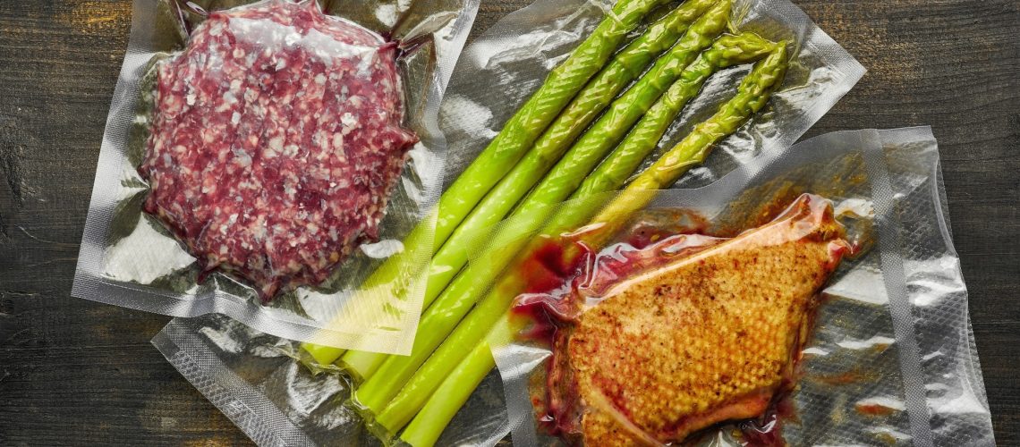 Duck breast, burger meat and asparagus vacuum sealed on wooden table