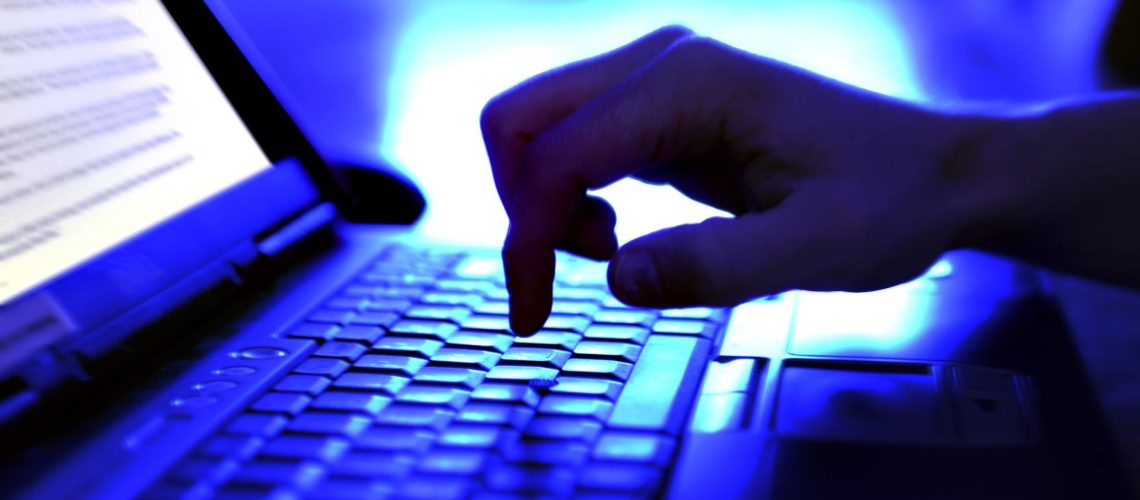A person typing on a laptop, bathed in blue light