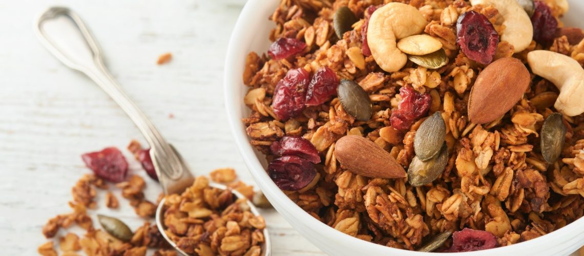 Homemade granola in glass jar with greek yogurt or milk and cashews, almonds, pumpkin with dried cranberry seeds