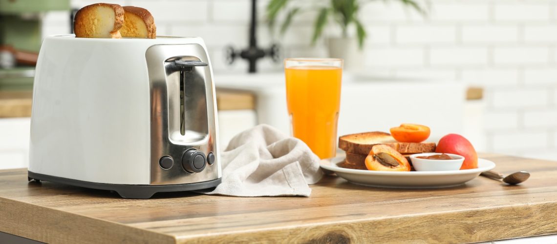 White toaster and plate with bread slices on wooden table in kitchen