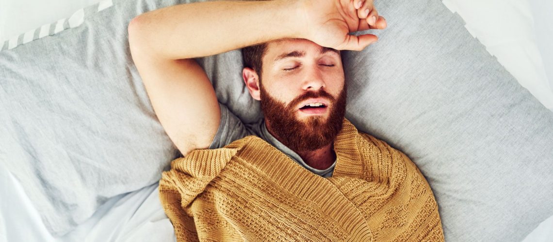 The image shows a man sleeping on his back with his mouth open and his arm above his head