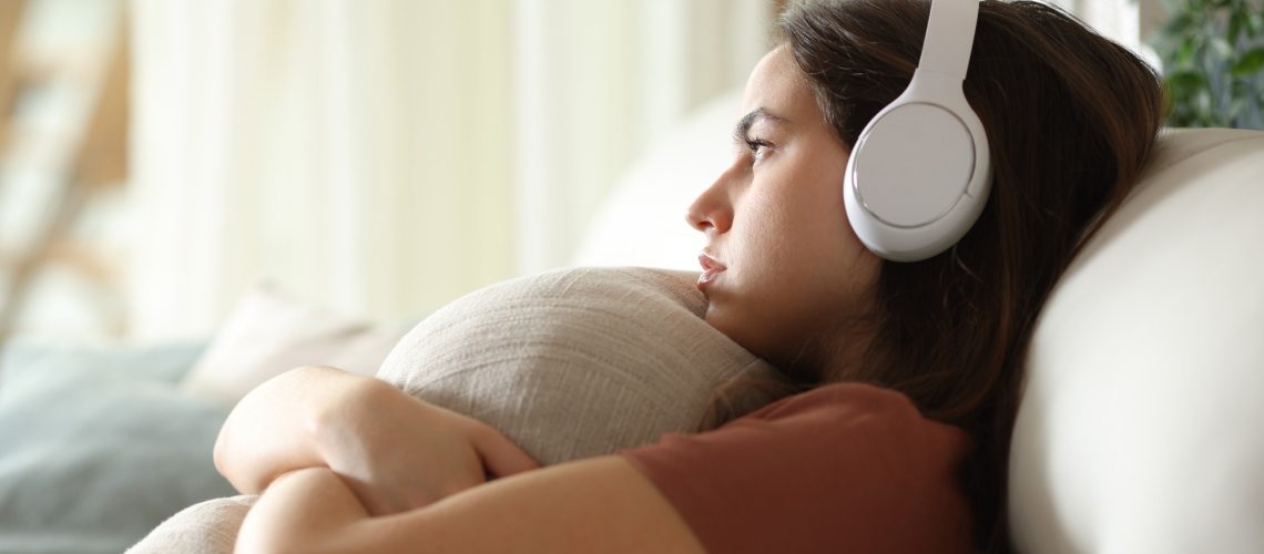Sad and melancholic woman listening music with headphone at home