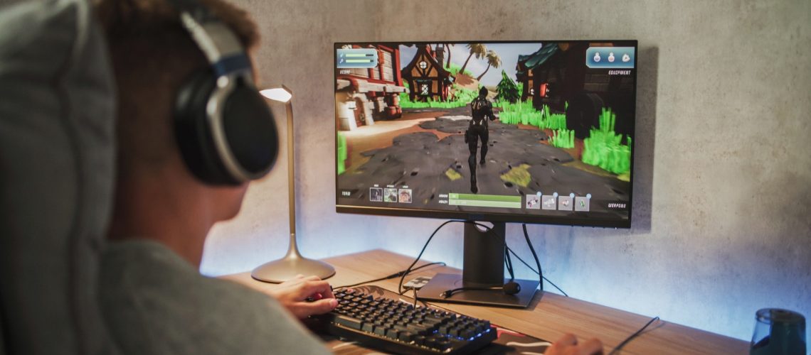 Caucasian teenager wearing headphones plays online video game on PC, spends leisure time at home.