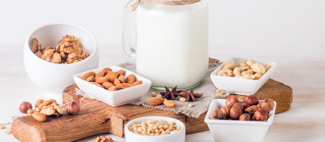 Vegan milk from nuts in glass jar with various nuts on white wooden background