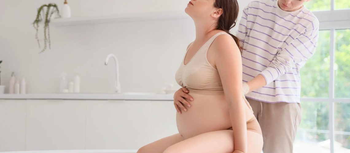 Young doula and pregnant woman sitting in bathtub at home
