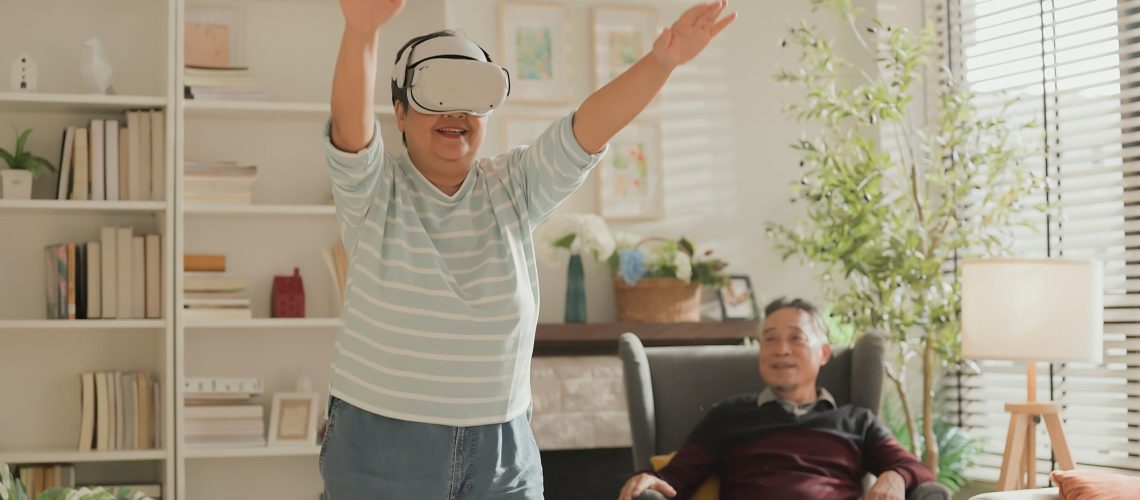Older adult couple in living room. Woman using VR experience to do gentle exercise movement