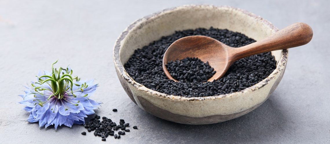 Black cumin seeds with nigella sativa flower on grey background