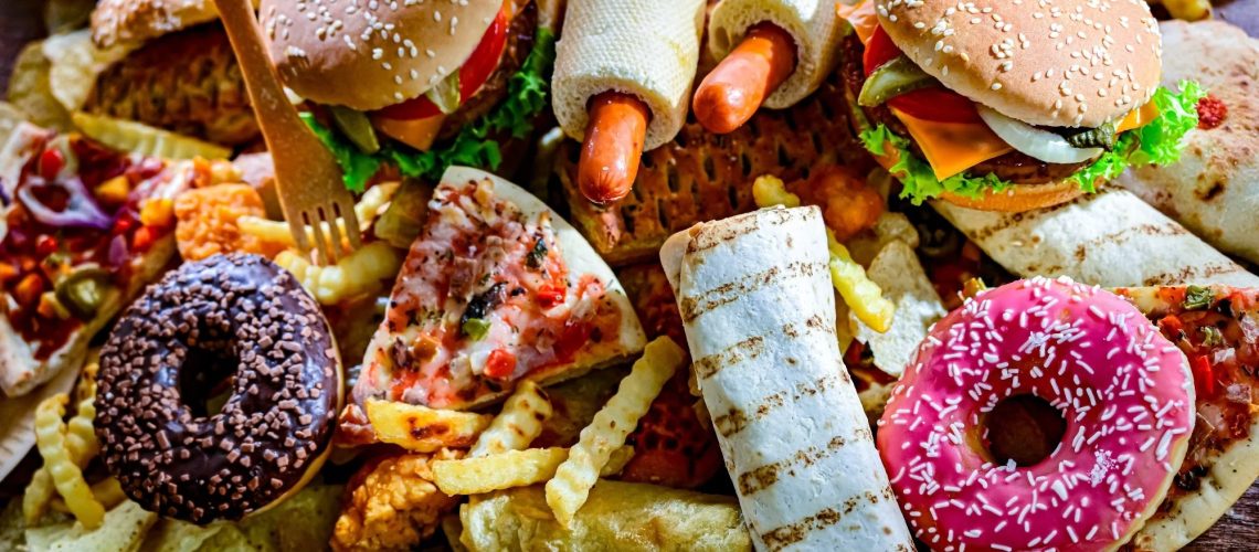 Assortment of ultraprocessed foods, including burgers, hot dogs, pizza, fries, and colorful doughnuts.
