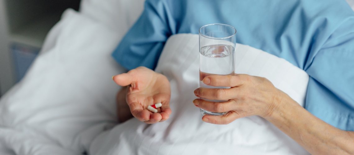 woman lying in bed and holding pills with glass of water in hospital