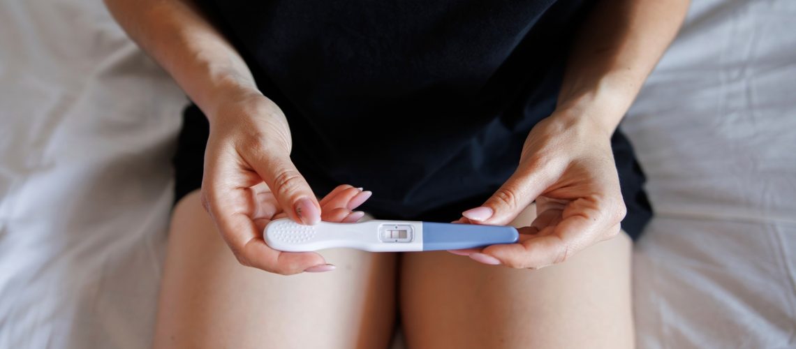 young woman holding pregnancy test sitting on bed
