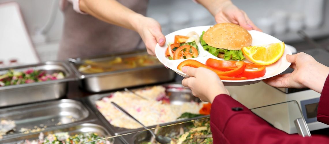 Pleasant woman giving lunch to school girl in cafeteria