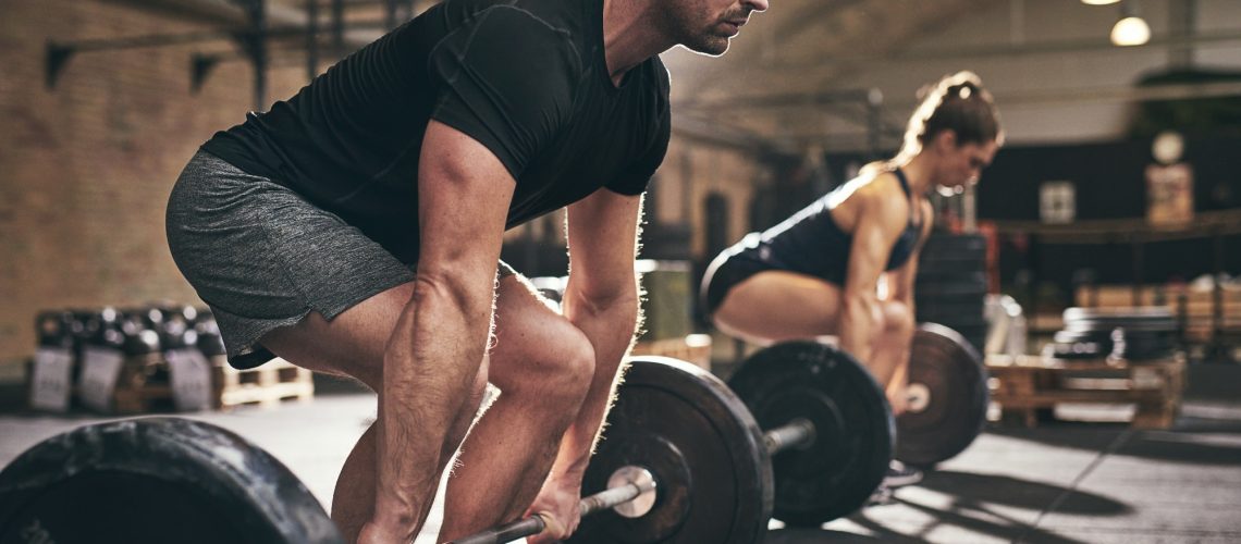 Sporty man and woman are about to lift barbells in gym