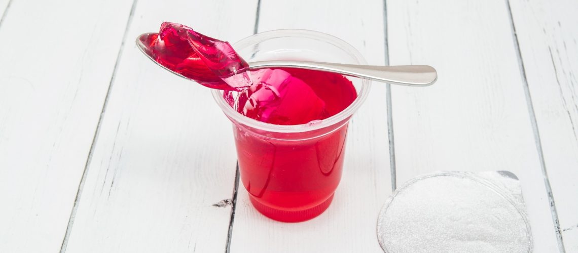 Plastic container for dairy foods with red clear jelly pudding with foil lid and spoon