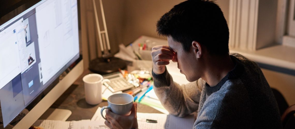 Man, studying and headache in night by computer for test, with coffee cup in his hand