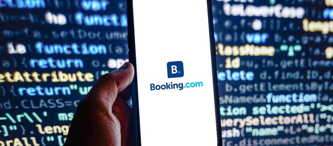 Booking.com logo on a smartphone in front of a screen of computer code