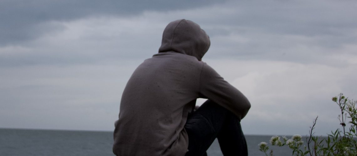 oneliness, a man looking towards the ocean during a cloudy weather