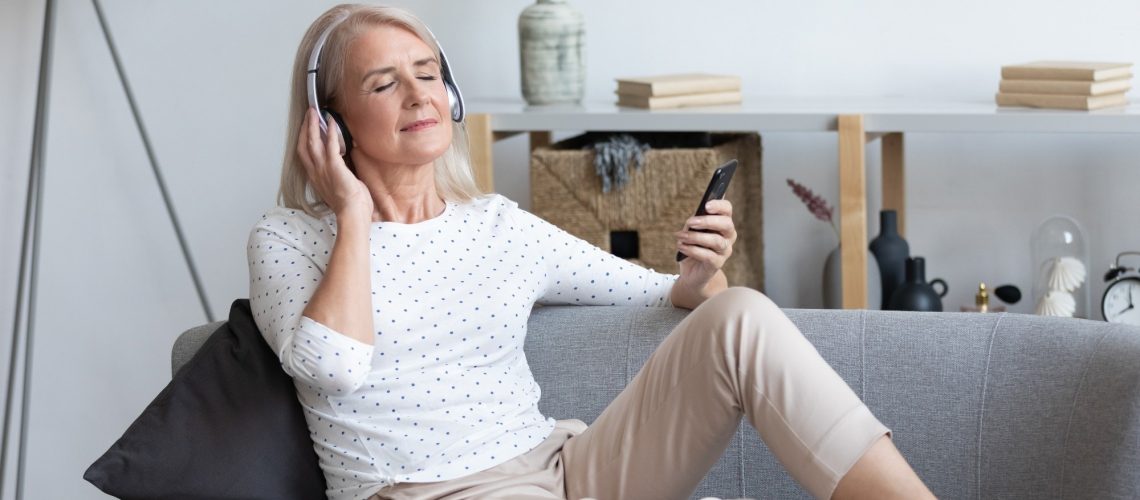 Older adult lady with headphones on, relaxed in sofa