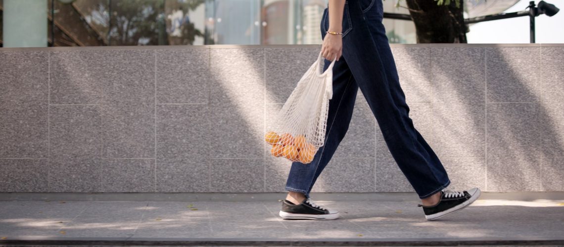 young woman walking carrying a shopping bag of oranges