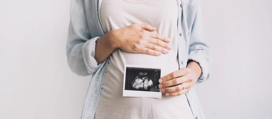 Pregnant woman holding ultrasound baby image. Close-up of pregnant belly and sonogram photo in hands of mother.