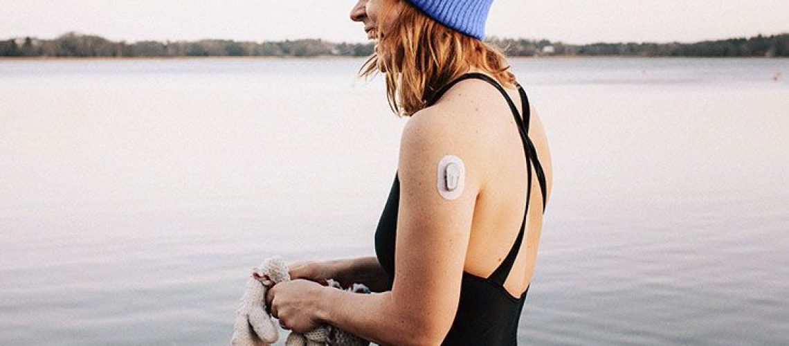 A woman wearing a glucose monitoring patch prepares to swim in a lake