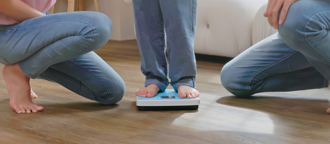 parents with their son in scale for weight measurement