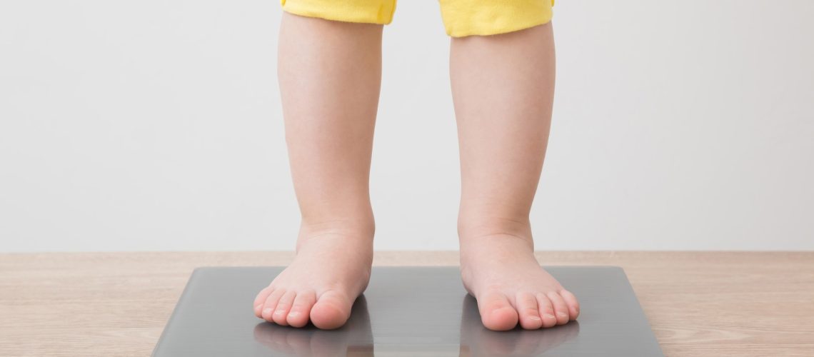 Baby girl with barefoot standing on weight scales