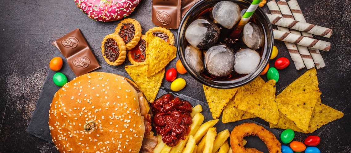 Burger, sweets, chips, chocolate, donuts, soda on a dark background.