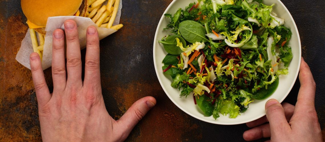 Young man making choice between salad and fast food