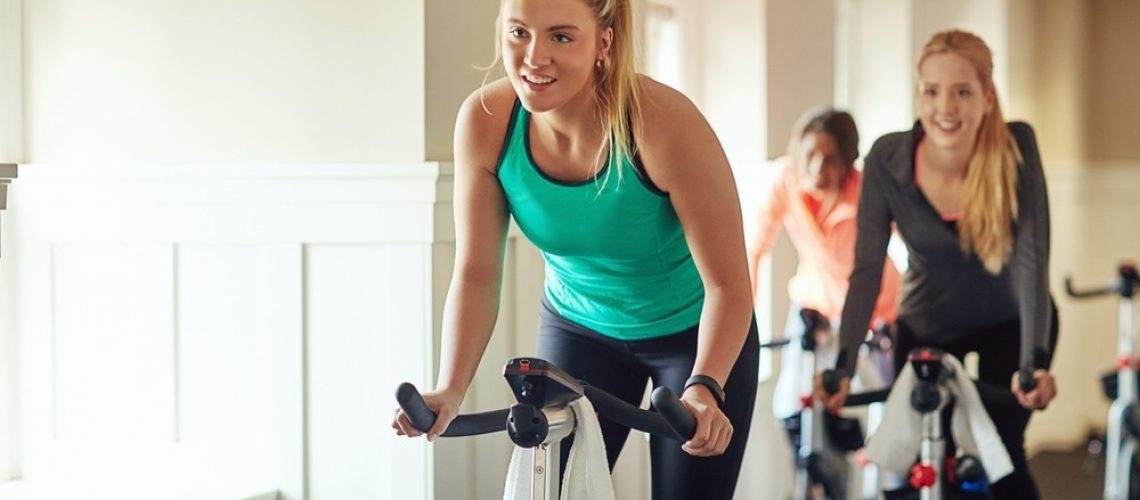 Female person, riding and stationary machine for workout challenge, aerobic instructor and equipment
