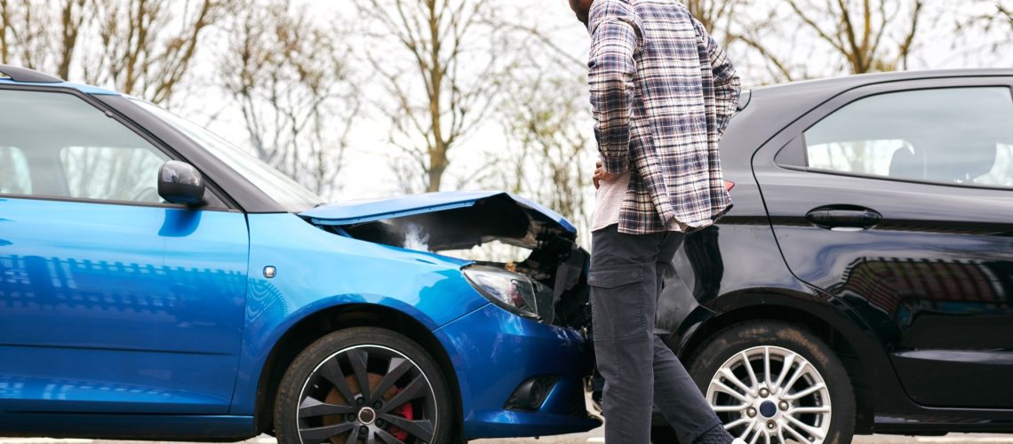 Young man looking at damaged car hit from behind after traffic accident