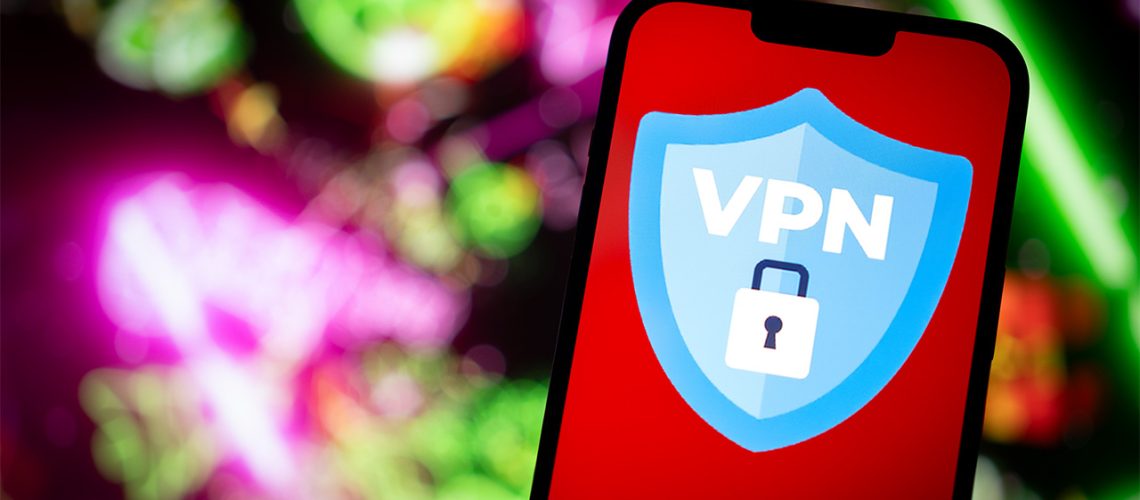 Smartphone displaying blue VPN shield logo with a padlock. There is a green and pink blurred technological background