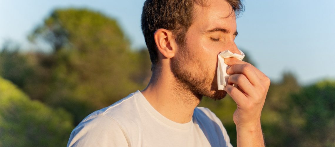 man surrounded by nature blowing his nose and sneezing for pollen allergy symptoms