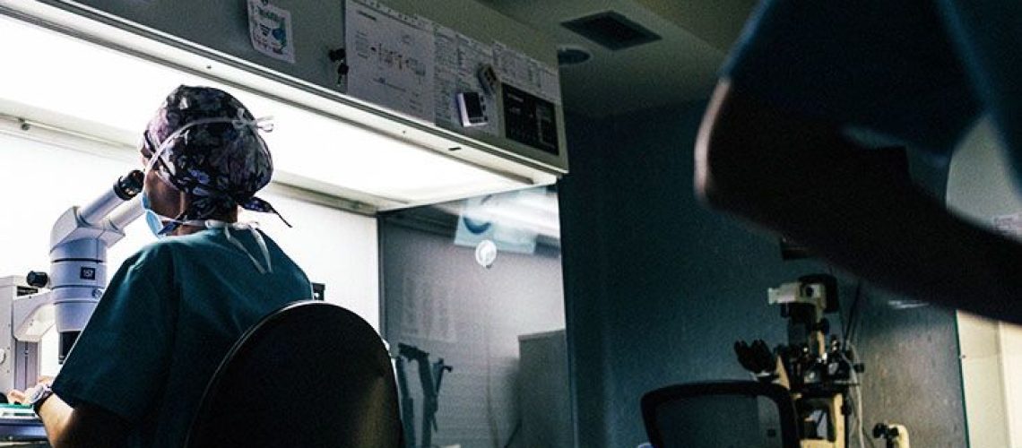 Scientist in lab examining cancer cells through microscope