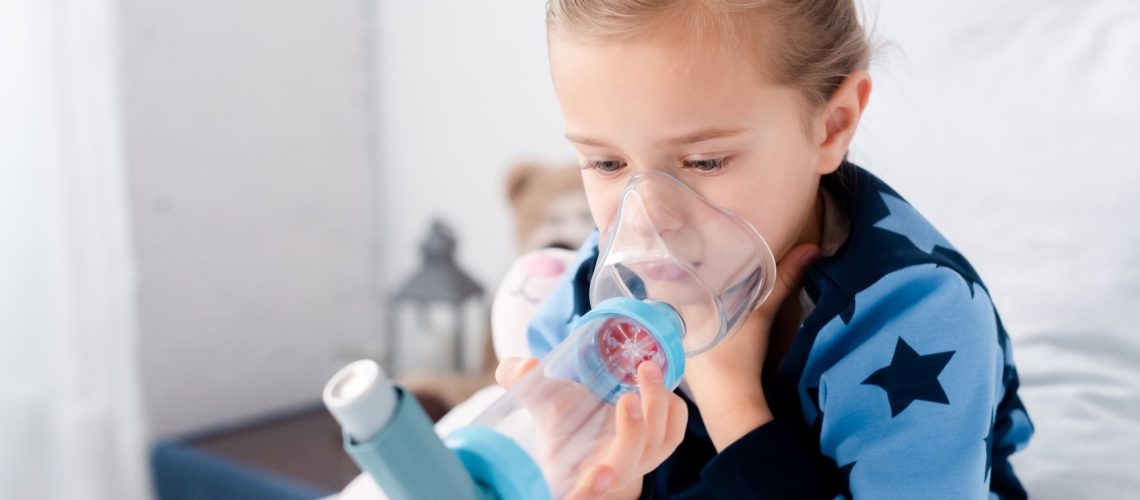 sick child using inhaler with spacer in bedroom